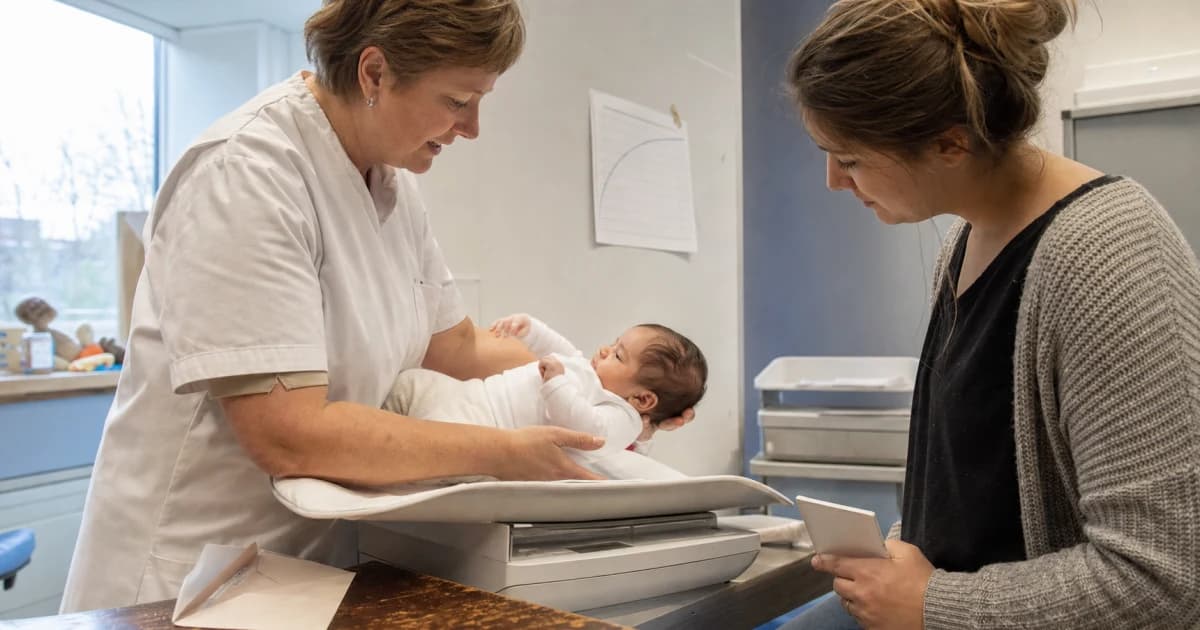 Een verpleegkundige weegt een baby op een babyweegschaal in het consultatiebureau terwijl een ouder een vaccinatieboekje vasthoudt, met een groeigrafiek aan de muur en een uitnodigingsbrief op tafel